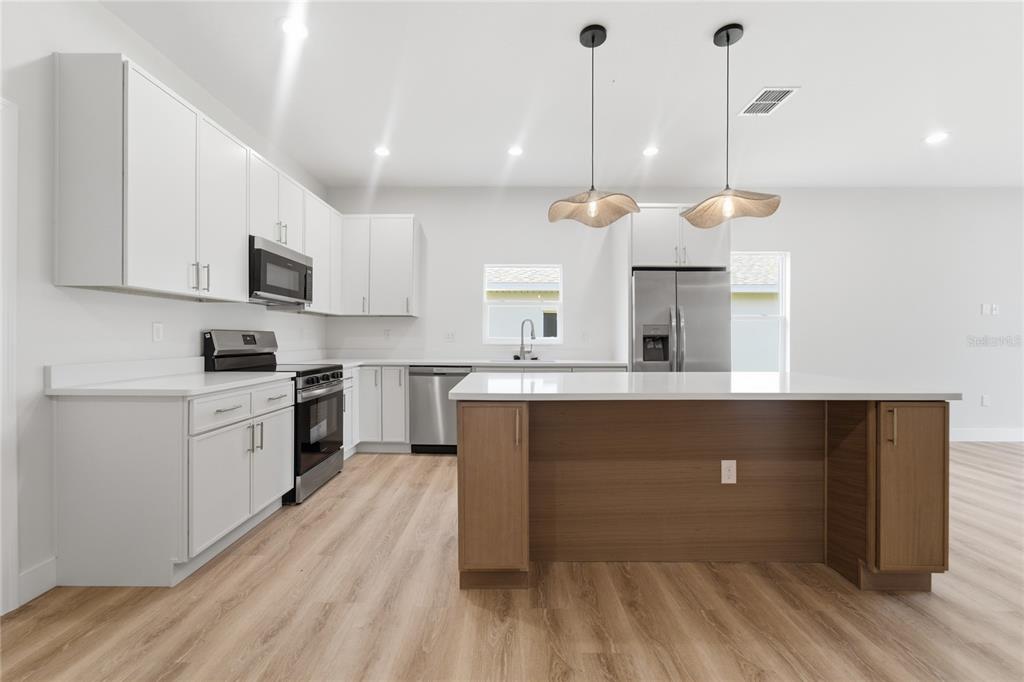 A modern kitchen features white cabinetry, stainless steel appliances, a wood-toned island, and light flooring — 1324 MARSHALL DRIVE, LEESBURG, FL