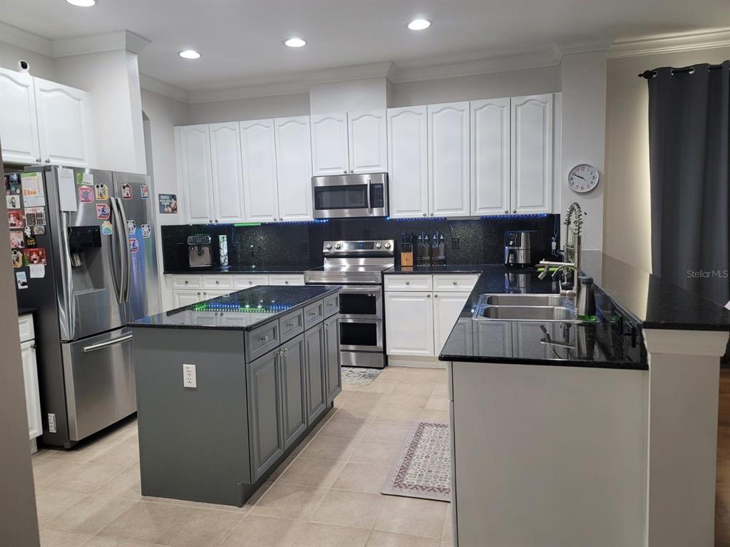 A kitchen features white cabinetry, a gray island, black countertops, and stainless steel appliances — 7011 NOBLETON DRIVE, WINDERMERE, FL
