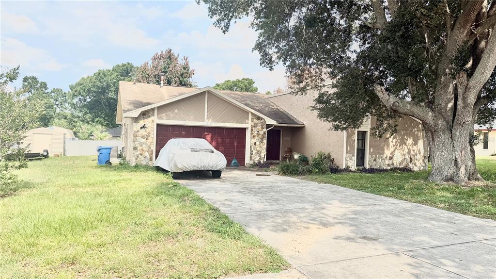 A single-story house with a stone-accented facade, a red garage door, and a large tree — 1406 MEADOW DRIVE NE, WINTER HAVEN, FL