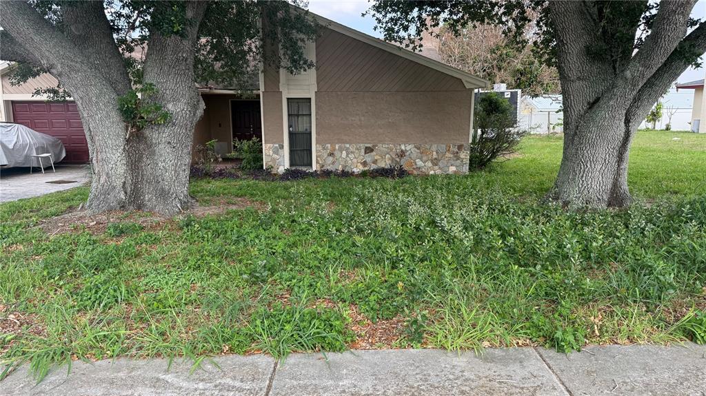A single-story house with a stone facade, two large trees, and an overgrown front yard — 1406 MEADOW DRIVE NE, WINTER HAVEN, FL