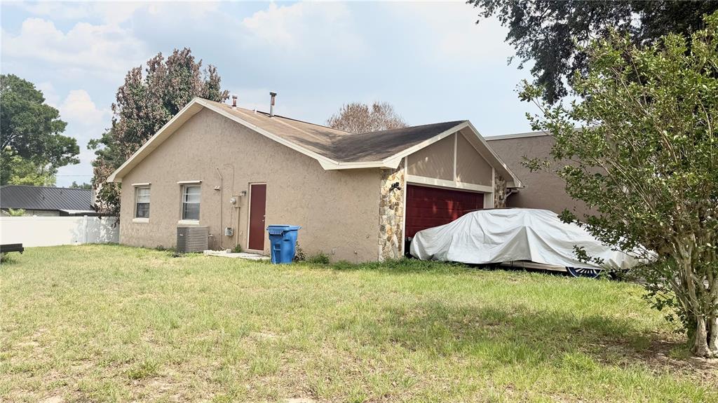 A tan stucco house with a red garage door and a car covered by a tarp — 1406 MEADOW DRIVE NE, WINTER HAVEN, FL
