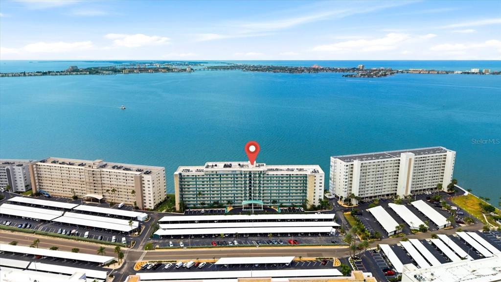 An aerial view shows three large apartment buildings with covered parking lots along a bay — 6020 SHORE BOULEVARD S UNIT 1002, GULFPORT, FL