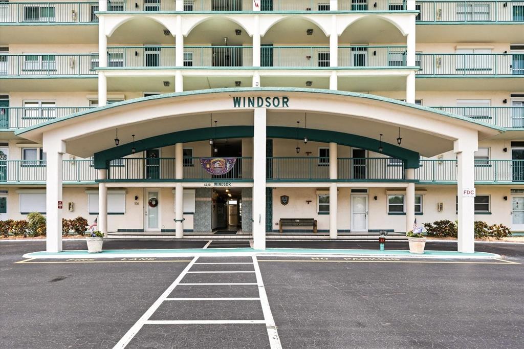 The exterior of a multi-story apartment building features a covered entrance with a Windsor sign — 6020 SHORE BOULEVARD S UNIT 1002, GULFPORT, FL