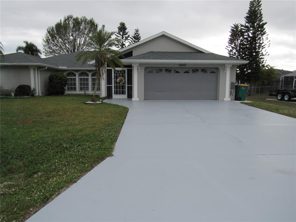 A single-story house with a gray garage, a paved driveway, and a front palm tree — 23081 AMBASSADOR AVENUE, PORT CHARLOTTE, FL