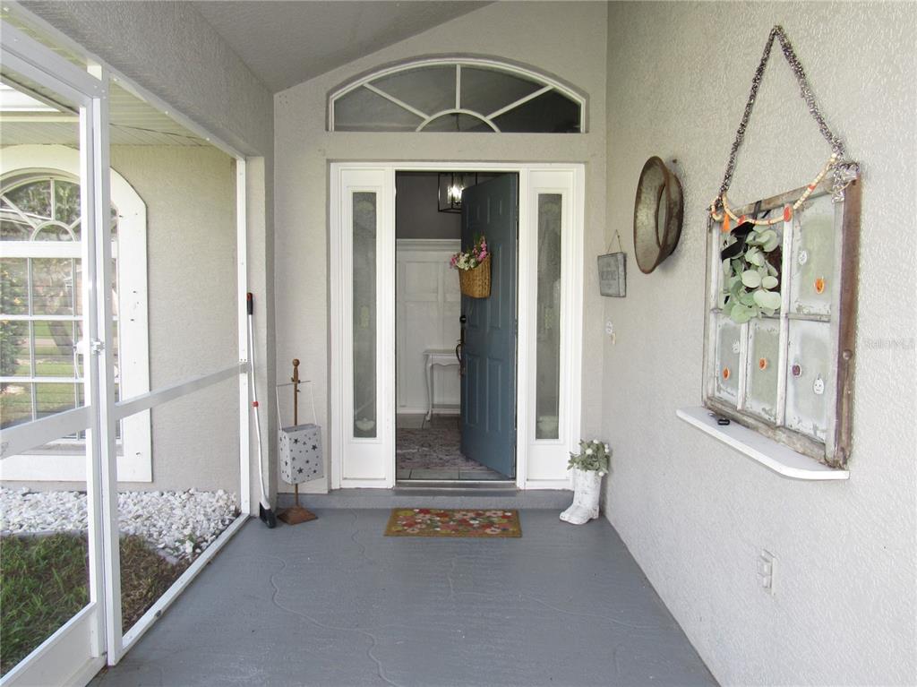 A covered entryway features a gray painted floor, a blue front door, and decorative wall hangings — 23081 AMBASSADOR AVENUE, PORT CHARLOTTE, FL