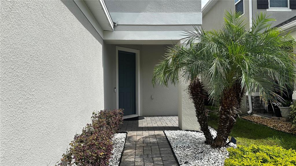 A paved walkway leads to a dark blue front door under a covered entryway — 1025 PANDO LOOP, ORLANDO, FL