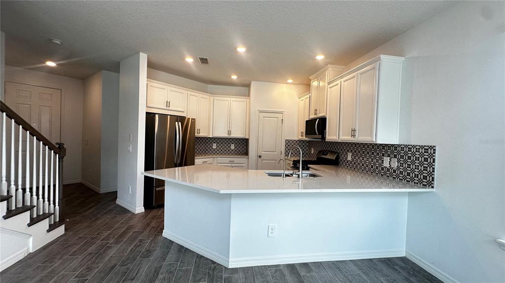 A kitchen features white cabinets, a quartz countertop, stainless steel appliances, and a tiled backsplash — 1025 PANDO LOOP, ORLANDO, FL