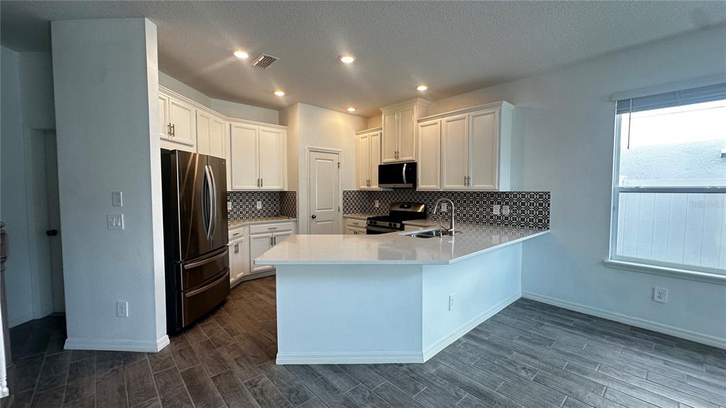 A kitchen features white cabinets, stainless steel appliances, a patterned backsplash, and a breakfast bar — 1025 PANDO LOOP, ORLANDO, FL