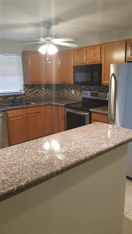 A kitchen features wood cabinets, granite countertops, stainless steel appliances, and a ceiling fan — 180 NE 12th Avenue # 17a, Hallandale Beach FL 33009, HALLANDALE BEACH, FL