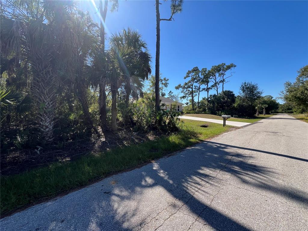 A paved road leads past a wooded lot toward a house in the distance — 23469 WICKENS AVENUE, PUNTA GORDA, FL