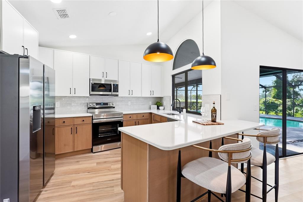A modern kitchen features white upper cabinets, wood lower cabinets, stainless steel appliances, and an island — 2889 HAMMOCK DRIVE, PLANT CITY, FL