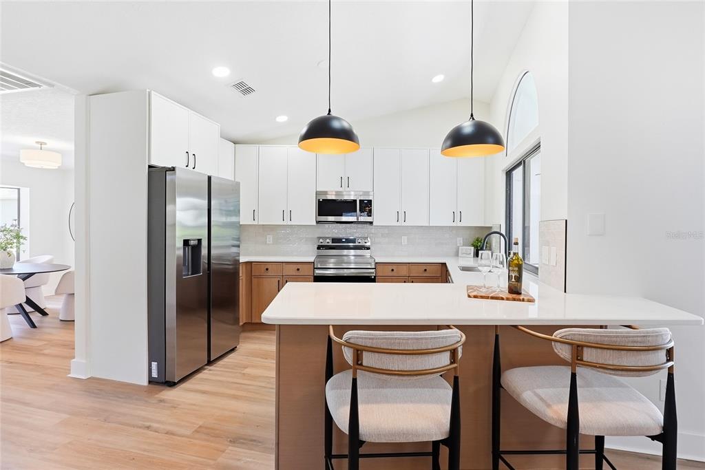 A modern kitchen features white upper cabinets, wood lower cabinets, stainless appliances, and a breakfast bar — 2889 HAMMOCK DRIVE, PLANT CITY, FL