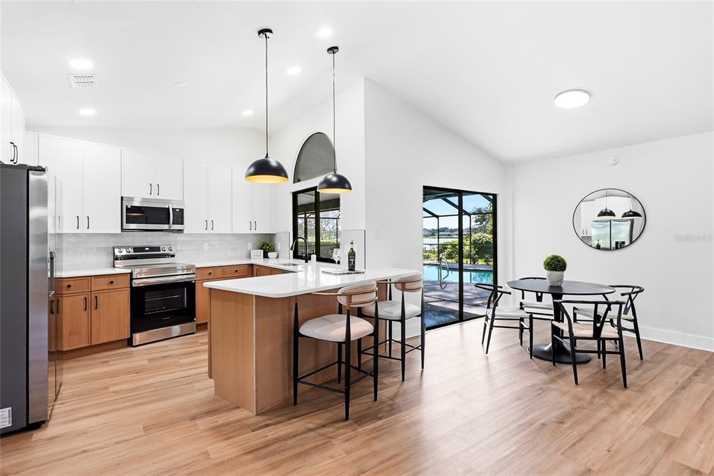 A modern kitchen features white upper cabinets, wood lower cabinets, a central island, and dining area — 2889 HAMMOCK DRIVE, PLANT CITY, FL