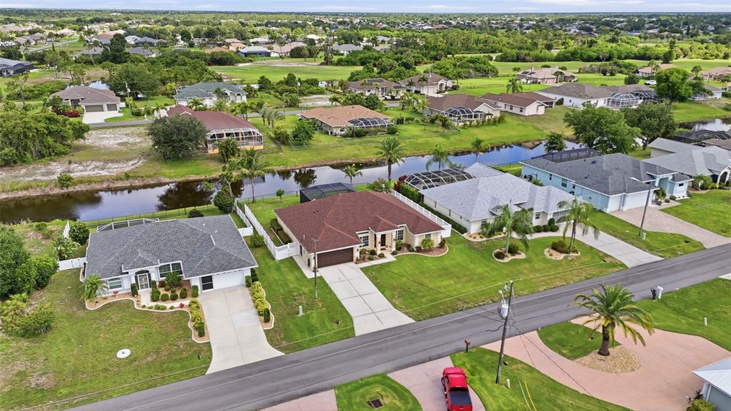 An aerial view shows several suburban houses with driveways and backyards along a canal — 11 MEDALIST LANE, ROTONDA WEST, FL