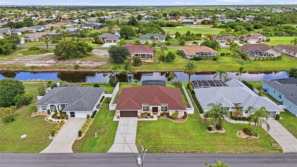 An aerial view shows three suburban houses with driveways and lawns bordering a narrow canal — 11 MEDALIST LANE, ROTONDA WEST, FL