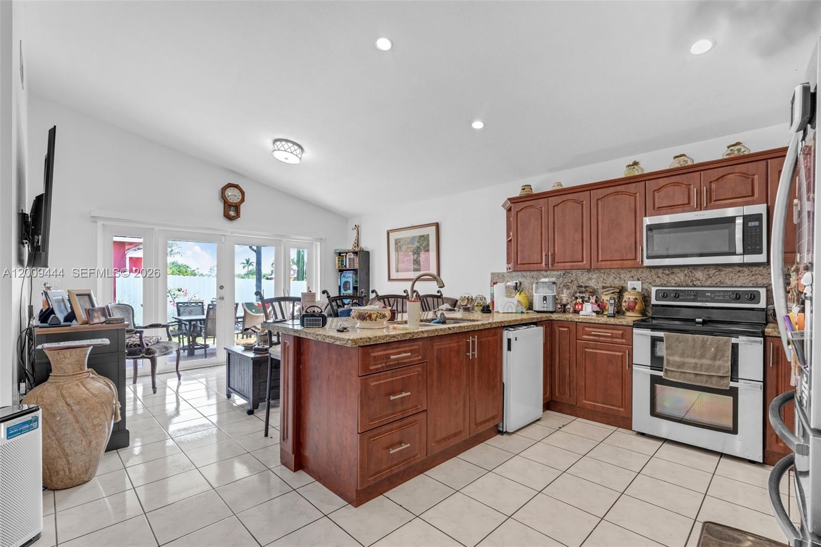 A kitchen with wooden cabinets, granite countertops, and a center island opens to a patio — 14240 SW 171st St, Miami FL 33177, MIAMI, FL
