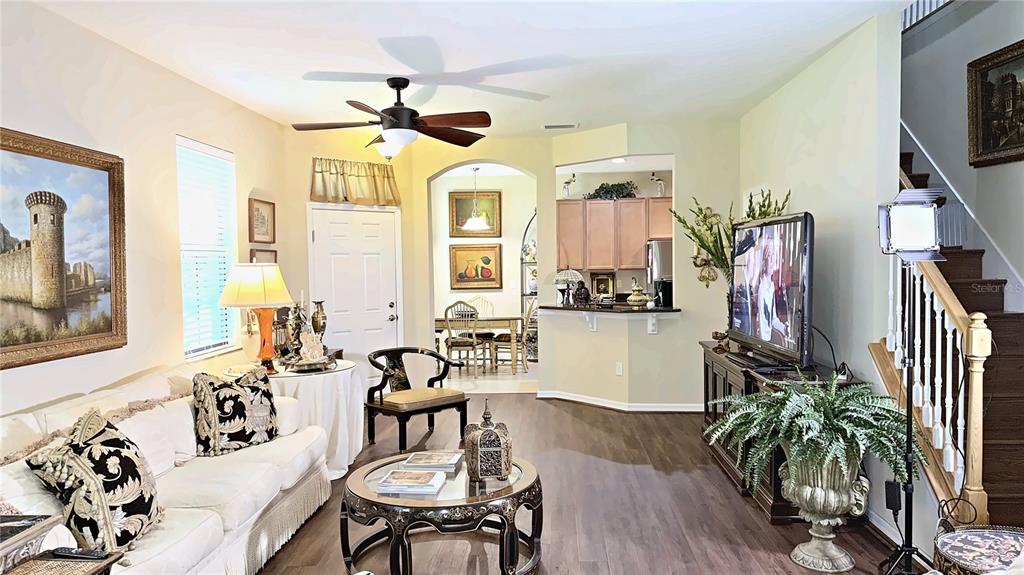 A living room features wood-look flooring, a ceiling fan, and an open view into the kitchen — 7974 TASSO COURT, SEMINOLE, FL
