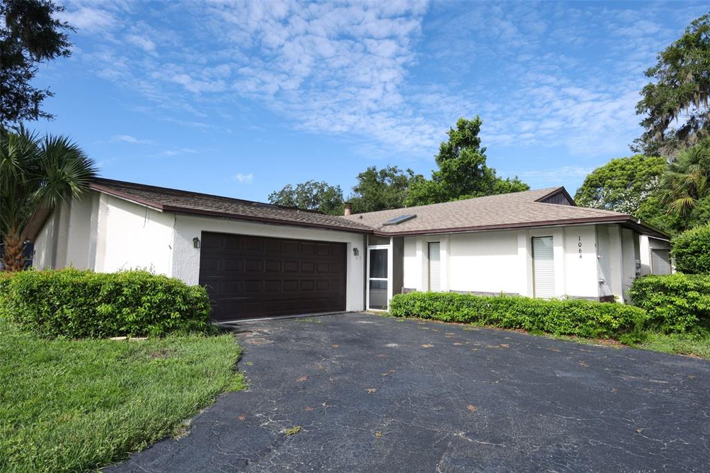 A single-story house with a dark garage door, white stucco walls, and a paved driveway — 1064 OLD MAGNOLIA COVE DRIVE, APOPKA, FL