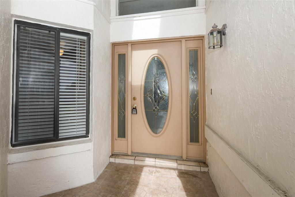 A beige front door with a glass oval insert sits beside a window with blinds — 1064 OLD MAGNOLIA COVE DRIVE, APOPKA, FL