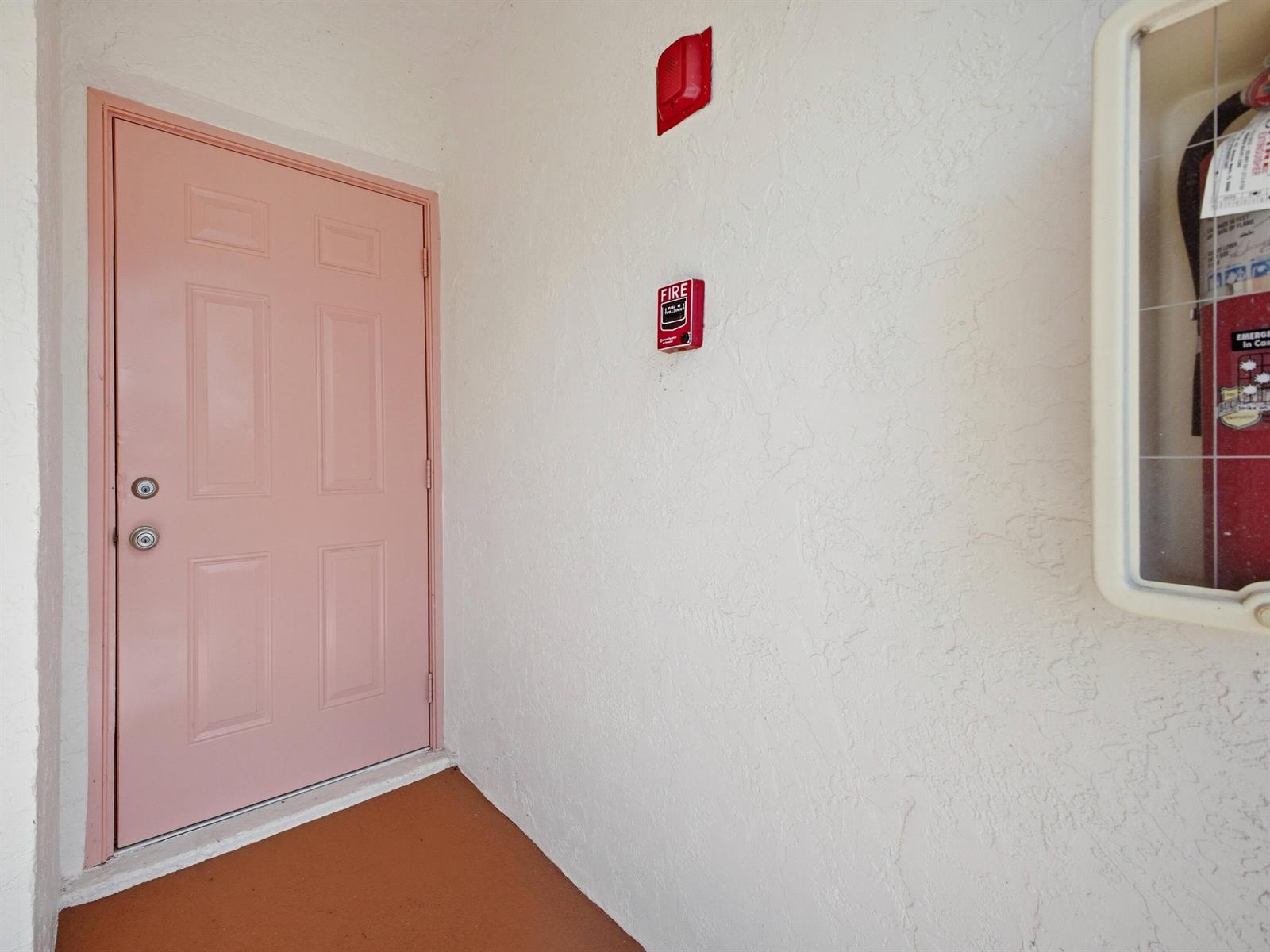 A pink door stands next to a fire alarm and a wall-mounted fire extinguisher cabinet — 321 Norwood Terrace # N221, Boca Raton FL 33431, BOCA RATON, FL