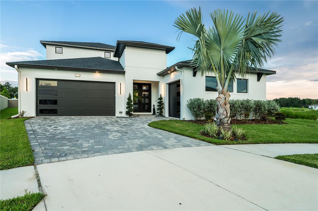 A modern two-story house with a white stucco exterior, dark garage doors, and a paved driveway — 32449 WETLAND BIRD VIEW, SAN ANTONIO, FL