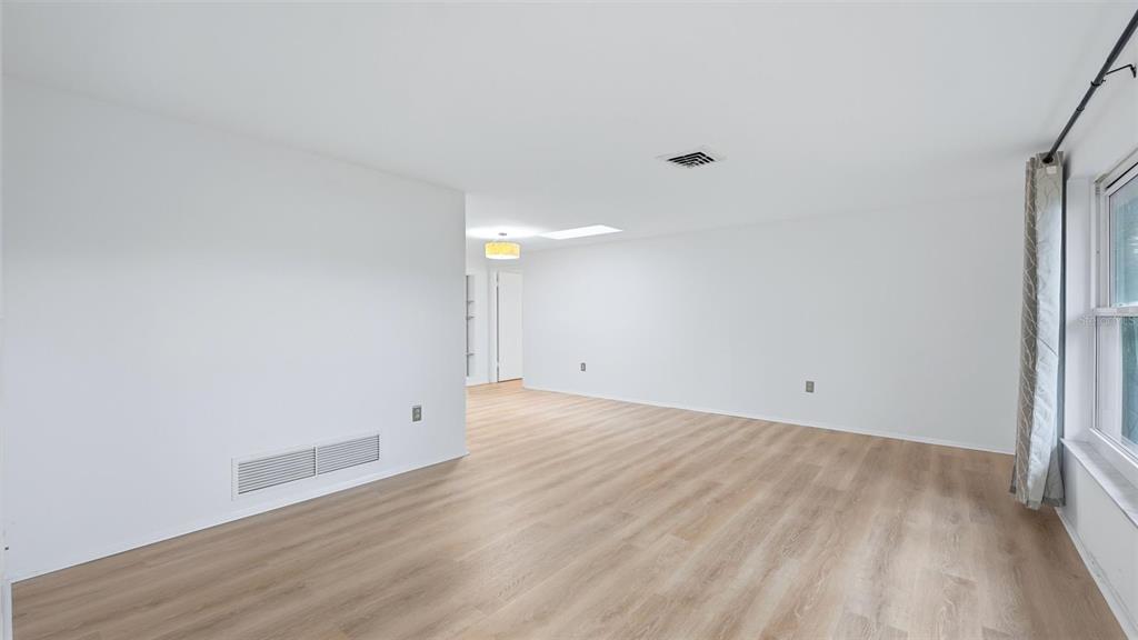 An empty living room with white walls, light wood-look flooring, and a large window — 1329 NANTUCKET ROAD, VENICE, FL