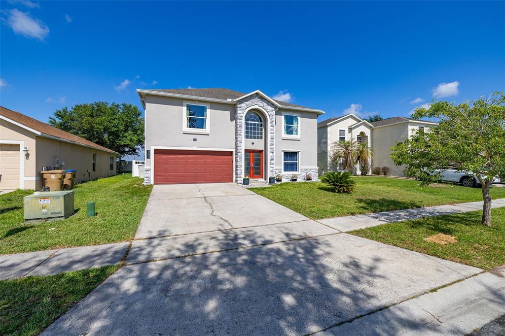 A two-story suburban house with a red garage door, stone facade, and concrete driveway — 5253 SUNSET CANYON DRIVE, KISSIMMEE, FL