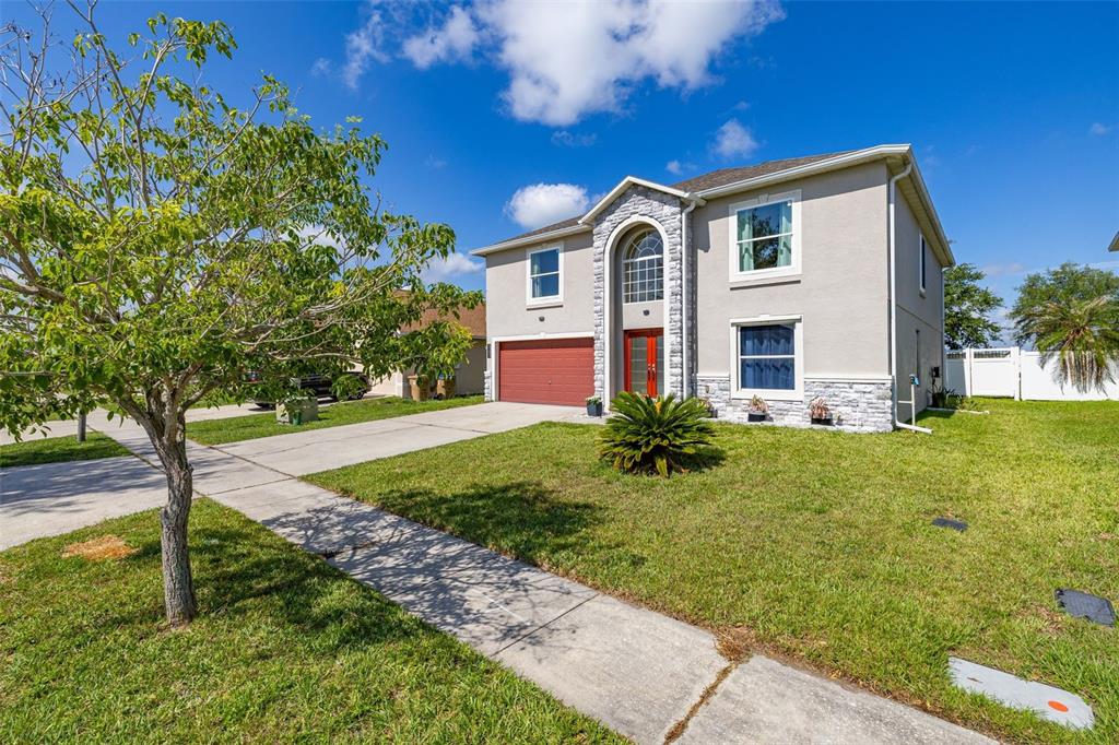 A two-story house with a red garage door, stone accents, and a front lawn — 5253 SUNSET CANYON DRIVE, KISSIMMEE, FL