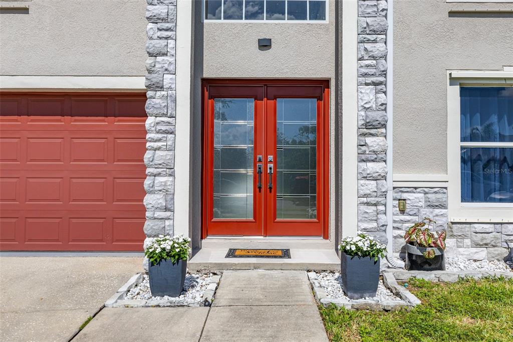 A red double front door with glass panels is flanked by stone accents and planters — 5253 SUNSET CANYON DRIVE, KISSIMMEE, FL