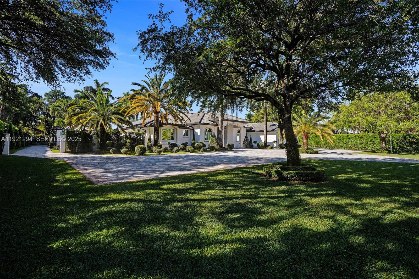 A white house with a paved driveway and palm trees sits behind a large tree — 10400 SW 62nd St, Miami FL 33173, MIAMI, FL