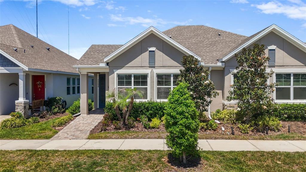 A single-story suburban house with a tan stucco exterior, shingled roof, and paved walkway — 13890 KINGFISHER GLEN DRIVE, LITHIA, FL