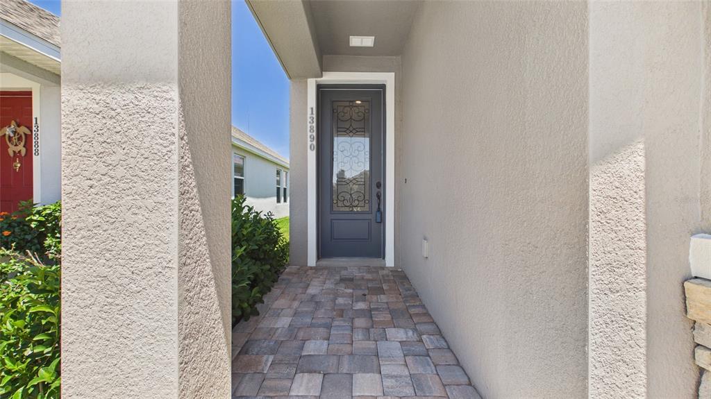 A paved walkway leads to a gray front door with decorative glass inserts — 13890 KINGFISHER GLEN DRIVE, LITHIA, FL