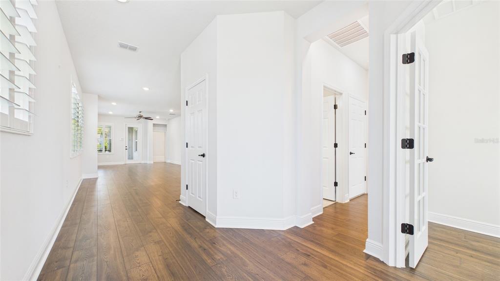 A hallway with wood-look flooring leads to an open living area with white walls — 13890 KINGFISHER GLEN DRIVE, LITHIA, FL
