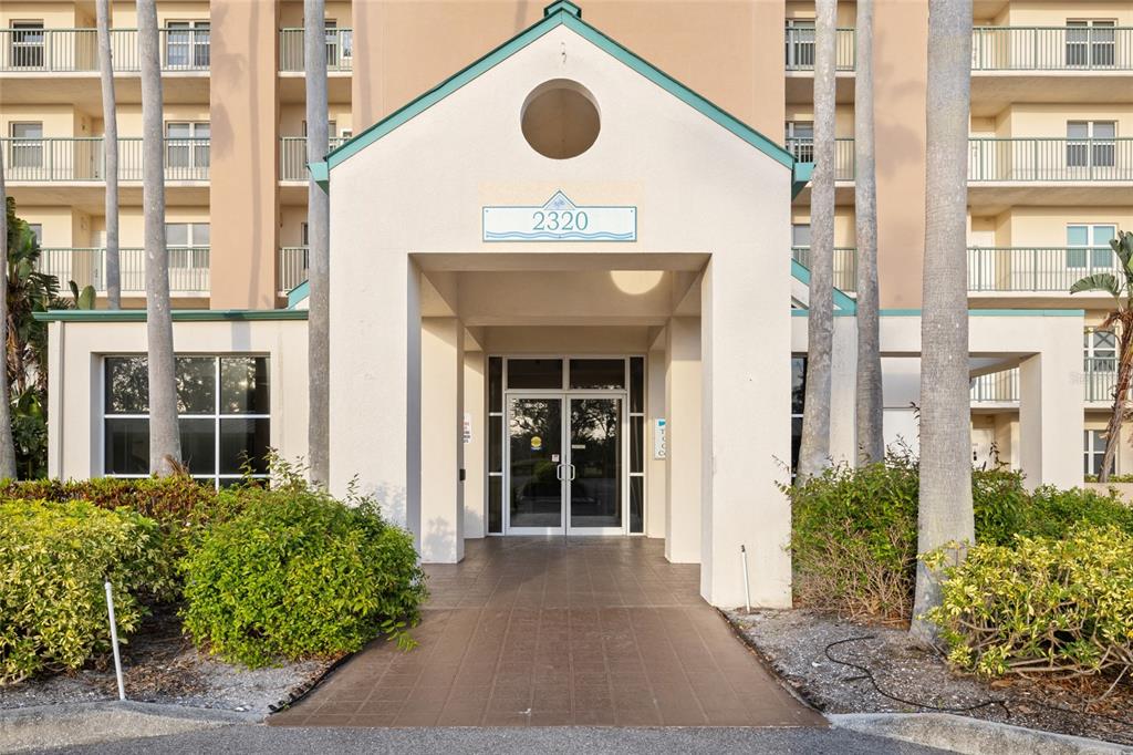 The exterior entrance of a multi-story apartment building features a covered walkway and glass doors — 2320 TERRA CEIA BAY BOULEVARD UNIT 206, PALMETTO, FL