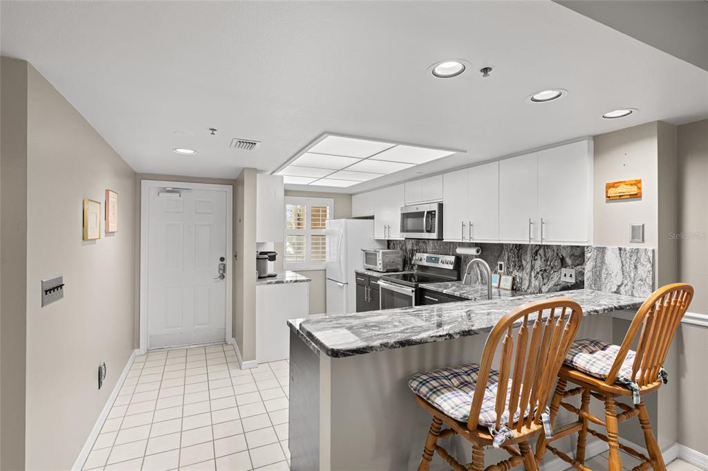 A kitchen with white cabinets, marble-patterned countertops, a breakfast bar, and tiled flooring — 2320 TERRA CEIA BAY BOULEVARD UNIT 206, PALMETTO, FL