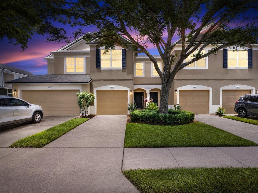 A two-story townhouse exterior with four garage doors, a large tree, and a concrete driveway — 4979 POND RIDGE DRIVE, RIVERVIEW, FL
