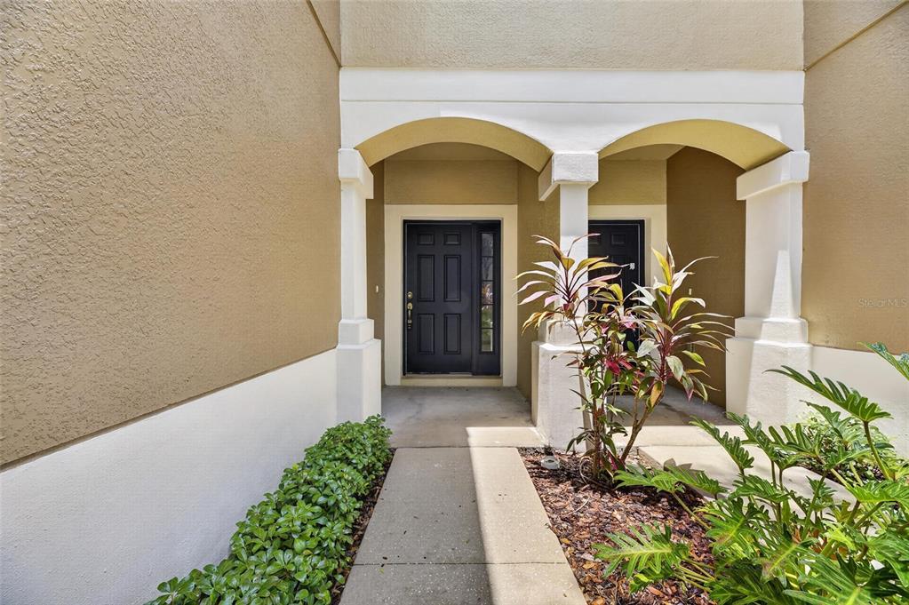 A covered entryway features a concrete walkway, a dark front door, and decorative pillars — 4979 POND RIDGE DRIVE, RIVERVIEW, FL