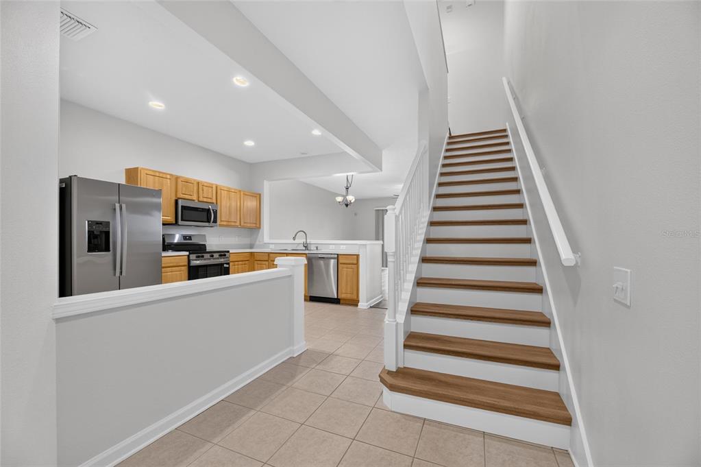 A kitchen with wood cabinets and stainless appliances sits beside a staircase with wood treads — 4979 POND RIDGE DRIVE, RIVERVIEW, FL