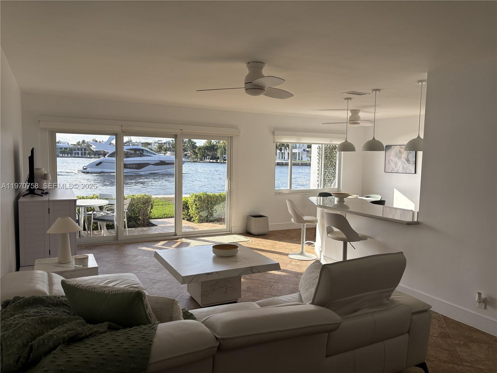 A living room with a white sectional, marble coffee table, and sliding doors overlooking a canal — 1201 S Riverside Dr # 107, Pompano Beach FL 33062, POMPANO BEACH, FL
