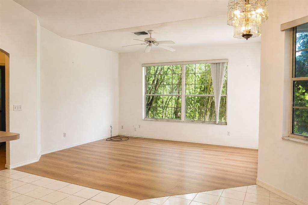 An empty living room features light wood-look flooring, white walls, a ceiling fan, and large windows — 7942 SW 103RD LOOP, OCALA, FL