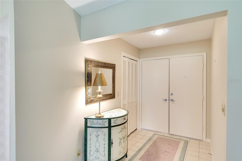 An entryway features a decorative console table with a lamp, a mirror, and double doors — 3825 WILSHIRE CIRCLE UNIT 1, SARASOTA, FL