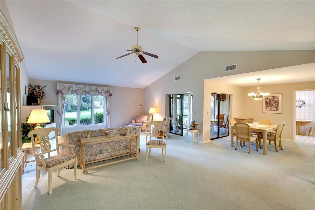 A living and dining area with vaulted ceilings, light carpeting, and sliding glass patio doors — 3825 WILSHIRE CIRCLE UNIT 1, SARASOTA, FL