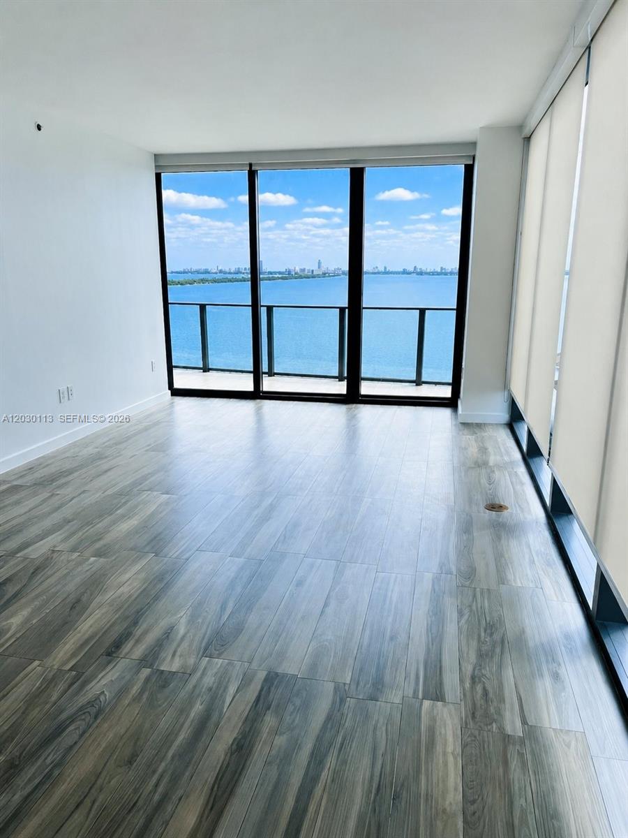 An empty room features wood-look tile flooring, floor-to-ceiling windows, and a view of water — 460 NE 28th St # 1408, Miami FL 33137, MIAMI, FL