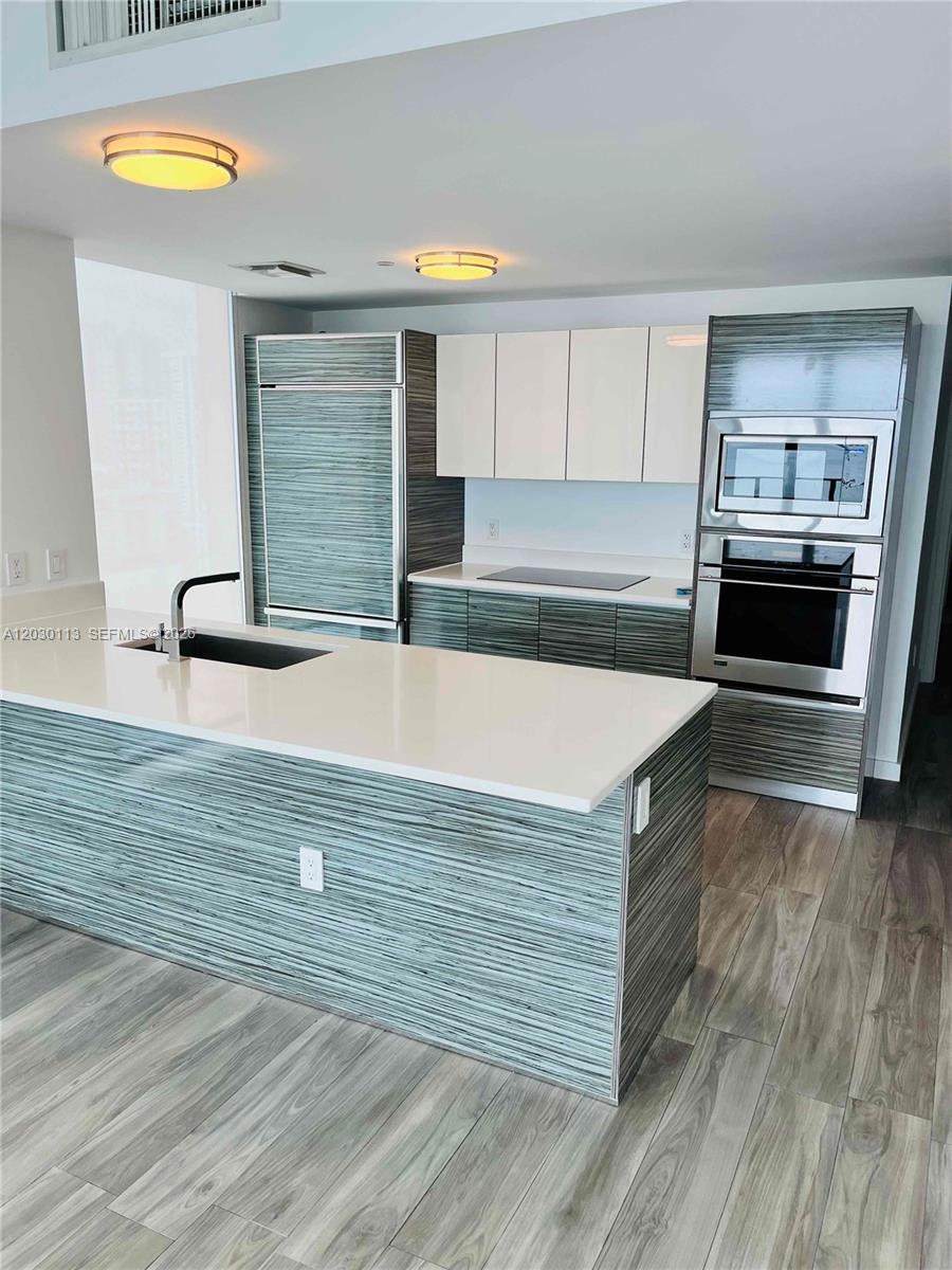 A modern kitchen features a white island, wood-grain cabinetry, and stainless steel built-in appliances — 460 NE 28th St # 1408, Miami FL 33137, MIAMI, FL