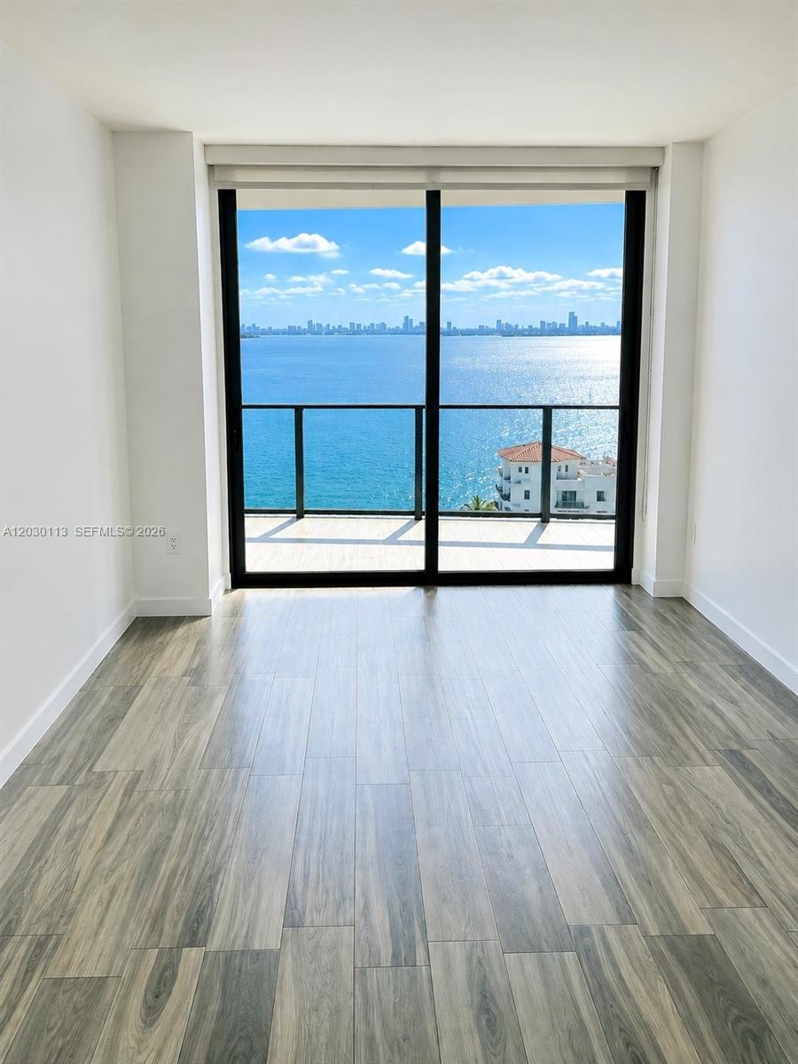 An empty room with wood-look tile flooring features a large sliding glass door overlooking water — 460 NE 28th St # 1408, Miami FL 33137, MIAMI, FL