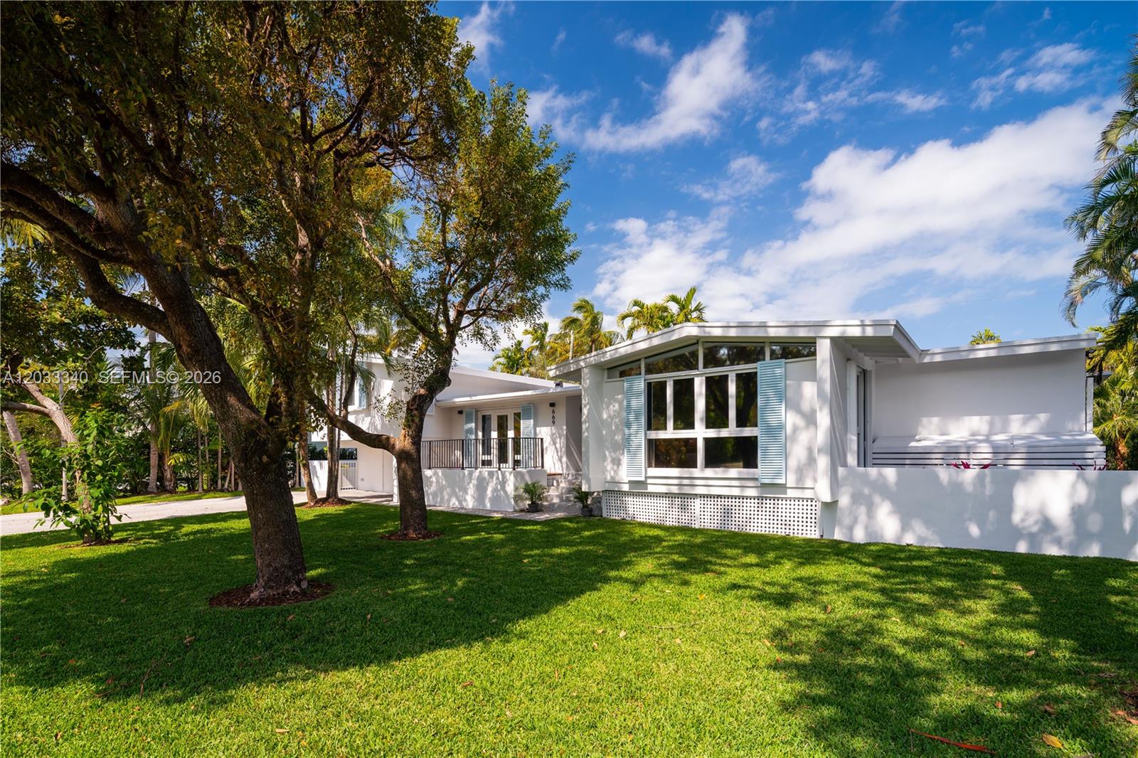 A white mid-century modern house with large windows and blue shutters sits on a lawn — 669 S Mashta Dr, Key Biscayne FL 33149, KEY BISCAYNE, FL