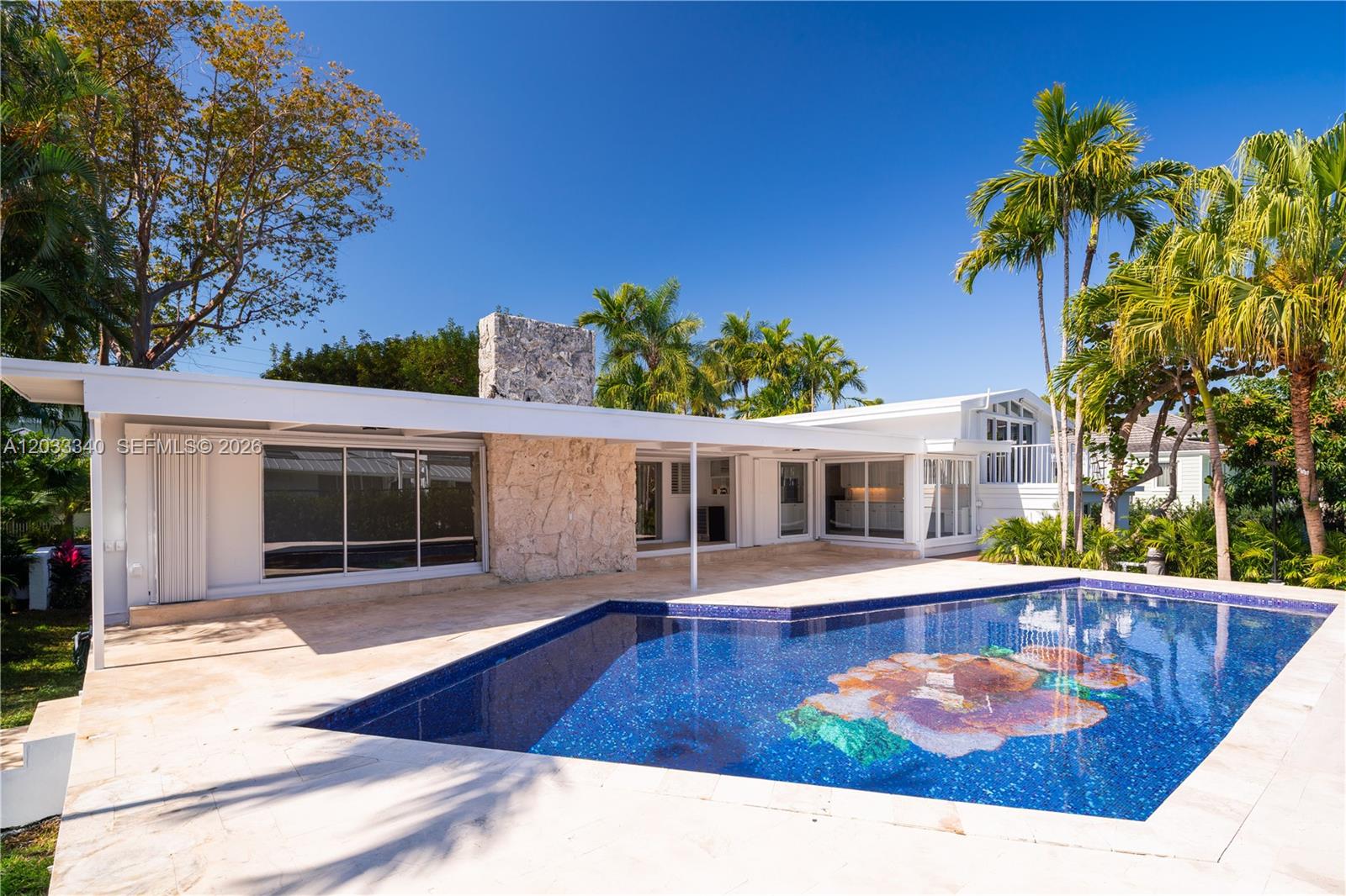 A swimming pool with a mosaic floor sits before a white house with stone accents — 669 S Mashta Dr, Key Biscayne FL 33149, KEY BISCAYNE, FL