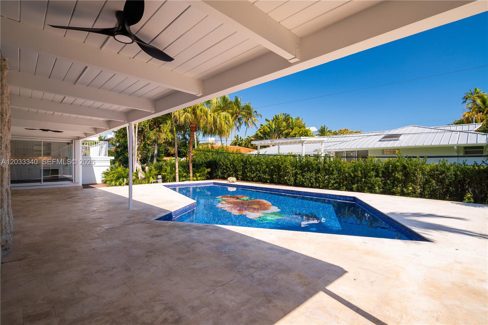 A covered patio with a ceiling fan overlooks a swimming pool with a floral mosaic — 669 S Mashta Dr, Key Biscayne FL 33149, KEY BISCAYNE, FL
