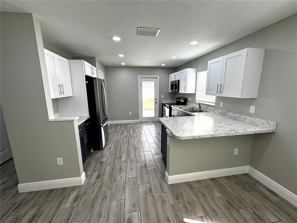 A kitchen features white cabinets, marble-look countertops, stainless steel appliances, and gray wood-look flooring — 5 OLIVE PLACE, OCALA, FL