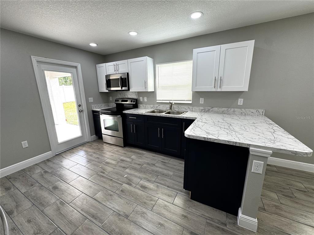 A kitchen features dark lower cabinets, white upper cabinets, marble-look countertops, and wood-look tile flooring — 5 OLIVE PLACE, OCALA, FL